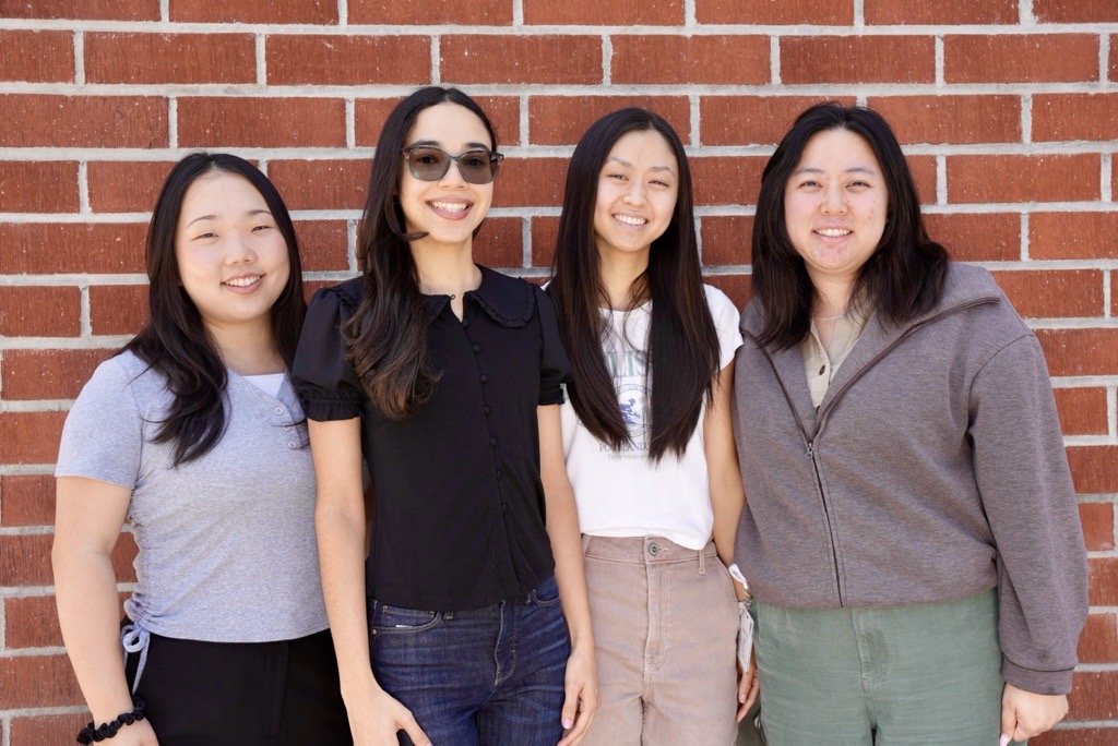 four students looking at camera standing in front of a brick wall