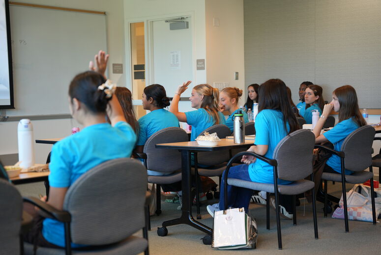 students at classroom desks and some have hands raised
