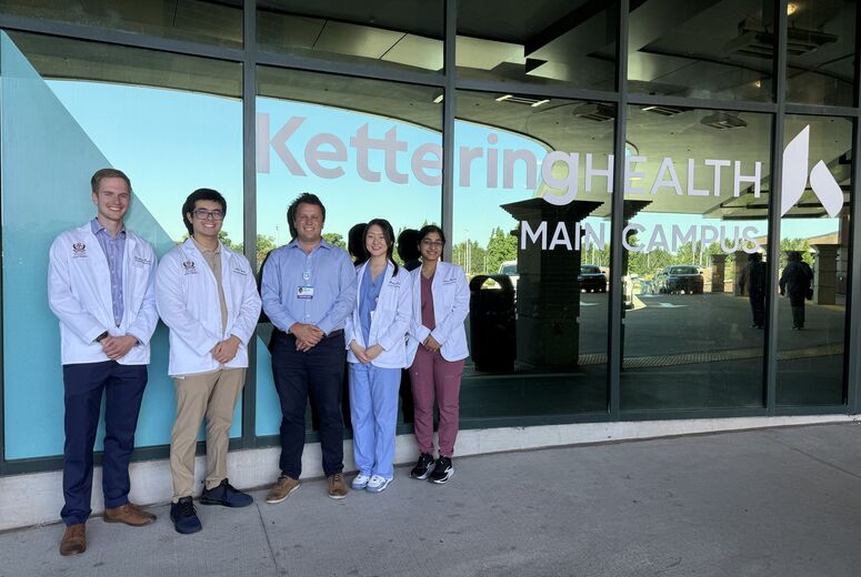 students with physician standing in front of windows at entrance of Kettering Health in dayton