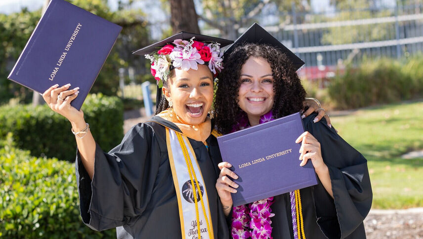 smiling graduates in regalia holding diplomas